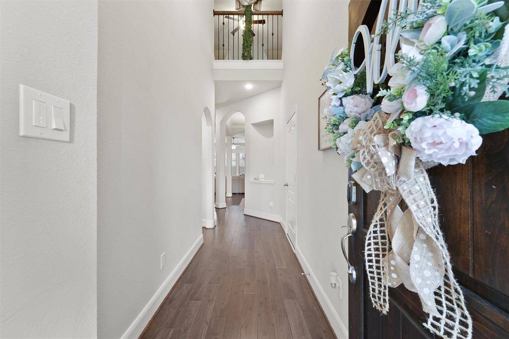 This photo shows a welcoming entryway with a floral wreath on the door, leading to a bright, open hallway with hardwood floors and high ceilings.