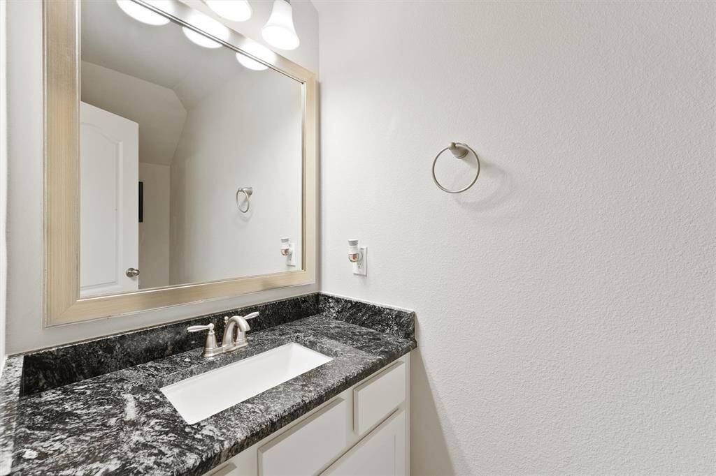 This photo showcases a modern bathroom with a sleek black granite countertop, an undermount sink, and a large framed mirror. The space is well-lit with contemporary fixtures and has a towel ring on the wall.