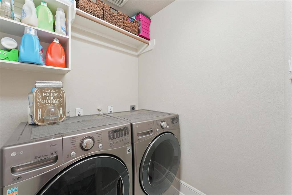 This photo shows a functional laundry room equipped with modern front-loading washer and dryer units. It features open shelving for laundry supplies and additional storage above. The space is clean and organized, ideal for efficient laundry tasks.