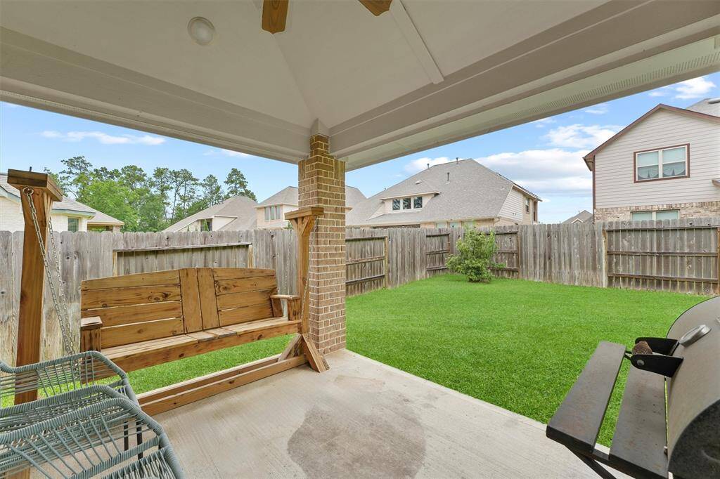 This photo shows a cozy covered patio with a wooden swing, overlooking a private, fenced backyard with lush green grass, perfect for relaxing and entertaining.