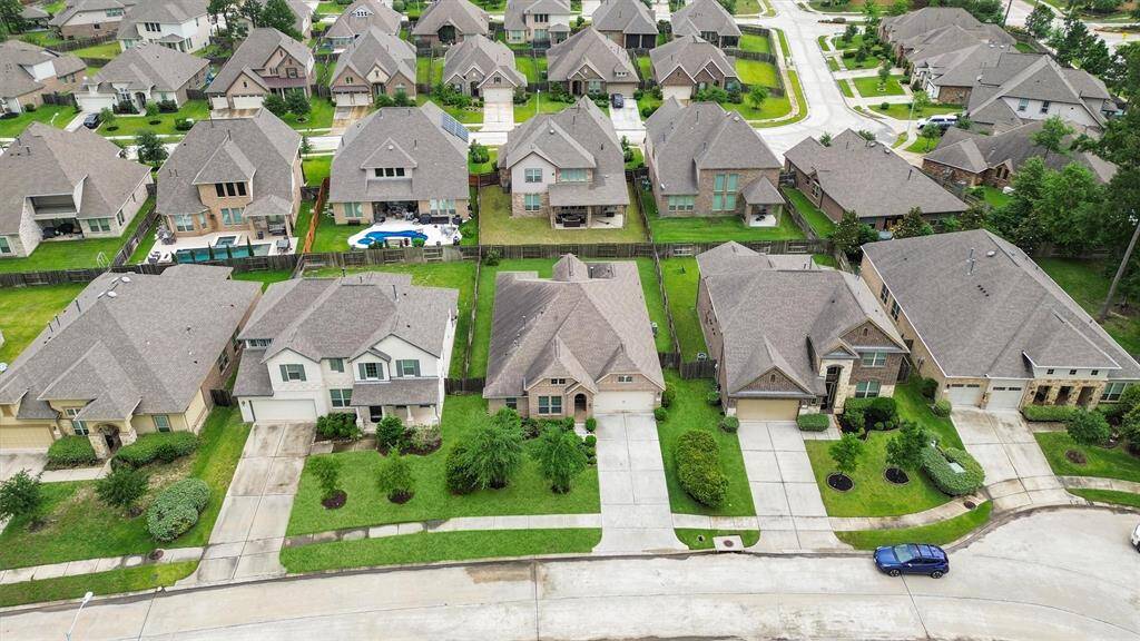 This aerial photo showcases a suburban neighborhood with well-maintained, similar-style homes, each featuring neatly landscaped lawns and driveways. The area appears quiet and family-friendly, with tree-lined streets and ample green space.