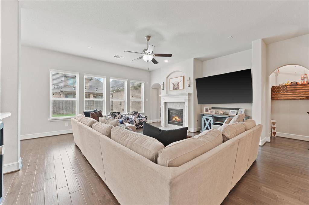 Spacious living room with abundant natural light, featuring a large sectional sofa, modern fireplace, wall-mounted TV, and elegant wood flooring.