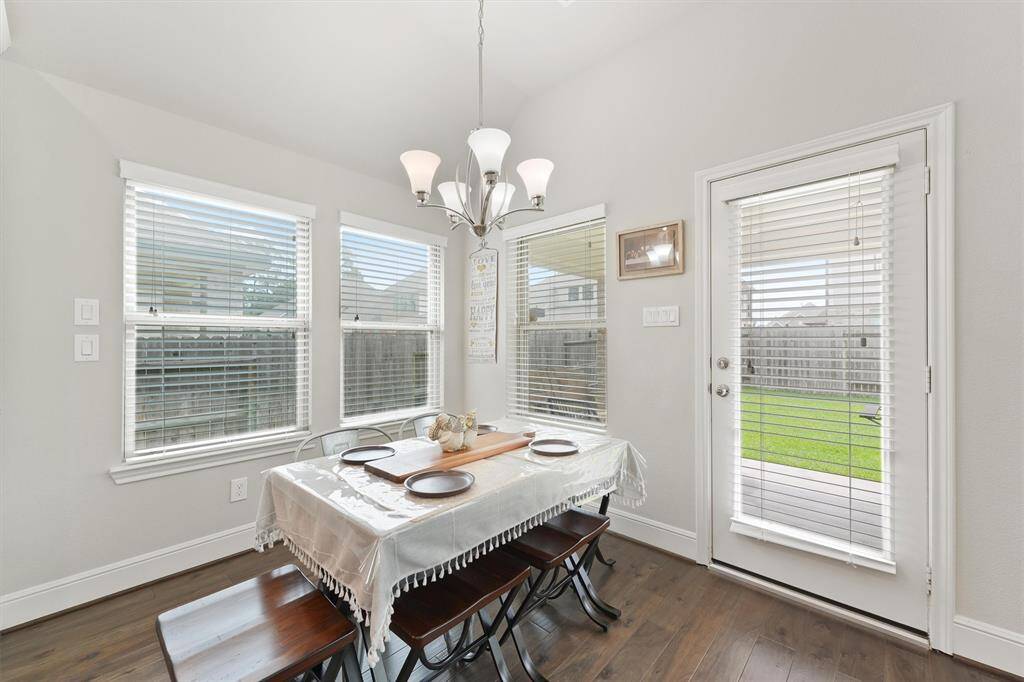 Bright dining area with large windows and a glass door leading to a backyard. Features hardwood floors, a modern chandelier, and seating for four.