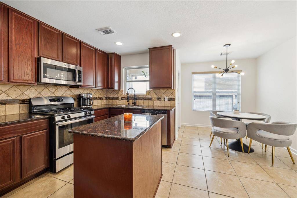 The island kitchen features rich wood cabinets, granite countertops and stainless steel appliances