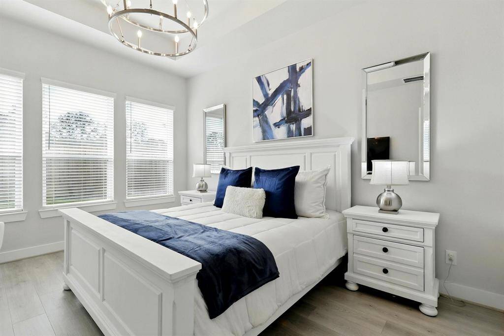 This elegant bathroom features a spacious walk-in shower with glass doors, a luxurious freestanding bathtub, and sleek, modern fixtures. The room is brightened by natural light from a large window with blinds, and the neutral tones  create a serene atmosphere.