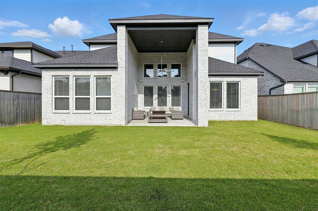 This spacious backyard  two-story home featuring a covered patio area. The exterior is light brick with large windows, offering a bright and inviting outdoor space ideal for relaxation and entertainment.