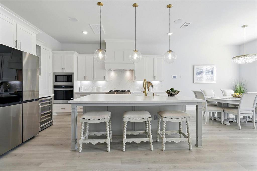 This kitchen features a sleek and modern design with white cabinetry, stainless steel appliances, and a spacious quartz island ideal for seating. Pendant lighting adds elegance,