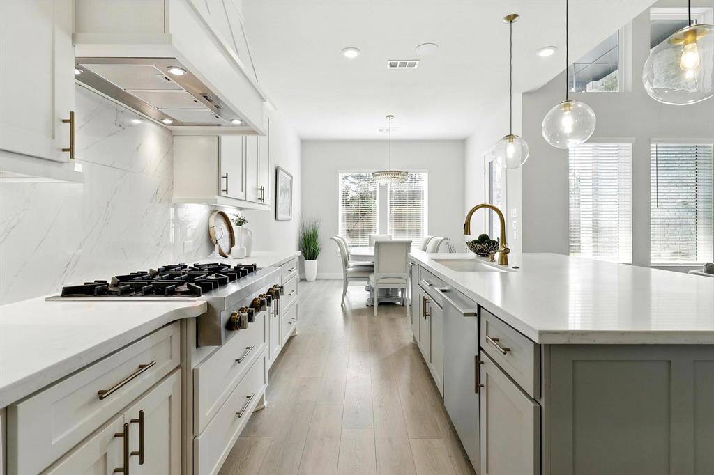 This kitchen features a modern design with white cabinetry, stainless steel appliances, Light wood flooring enhances the airy, contemporary feel.
