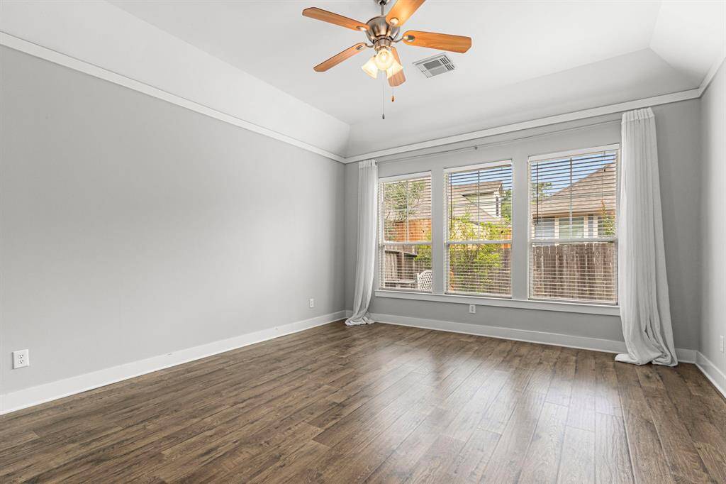 The primary bedroom features large windows with blinds and curtains, offering plenty of natural light. It has a ceiling fan and wood-look flooring, creating a warm and inviting atmosphere.
