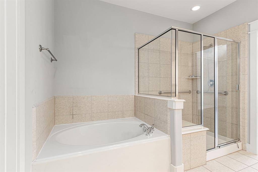This photo shows the primary bathroom with a separate glass-enclosed shower and a large soaking tub. The walls are tiled, and the space is bright and clean, offering a luxurious feel.