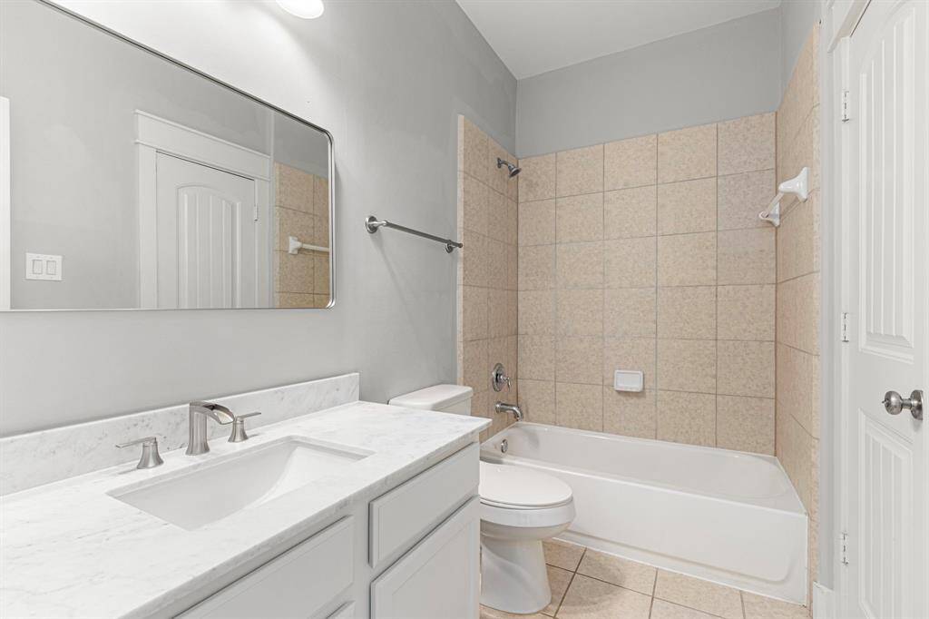This bathroom features a clean design with a white vanity and marble countertop, a large mirror, and neutral tile surrounding the bathtub. It offers a bright and spacious feel, ideal for a contemporary home.