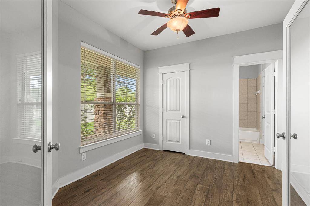 This room features a ceiling fan ample natural light from large windows with blinds. It includes a door leading to a tiled bathroom, enhancing convenience and functionality.
