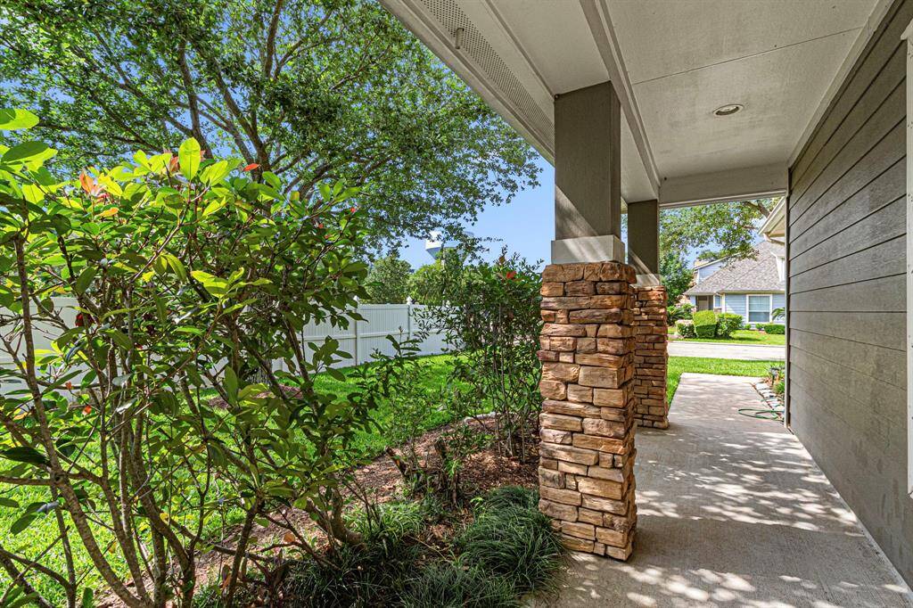 This photo showcases a charming front porch with stone pillars, surrounded by lush greenery and a well-maintained lawn. It offers a welcoming and serene outdoor space.