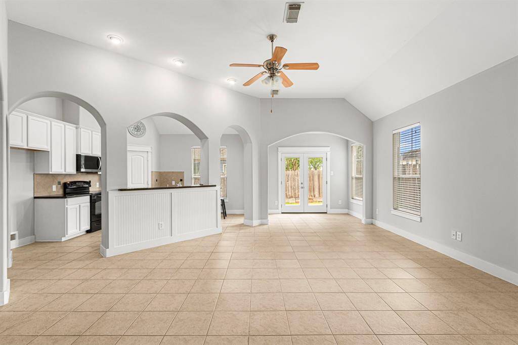 Spacious open-concept living area with high ceilings, neutral tile flooring, and abundant natural light. Features a modern kitchen with white cabinetry and a cozy dining nook. French doors lead to a private backyard.