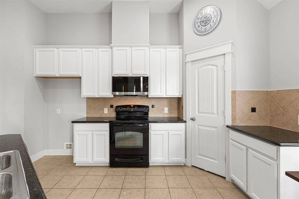 This kitchen features sleek appliances, white cabinetry, and a neutral tile backsplash. It includes ample counter space and a pantry, creating a functional and modern cooking area.