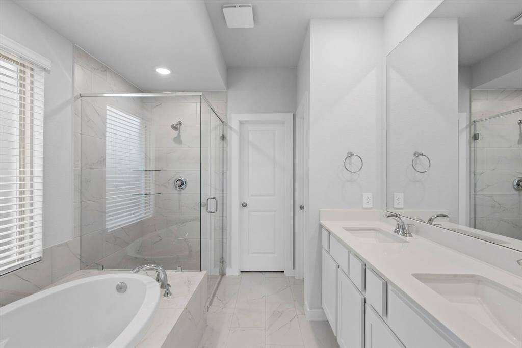 View of the primary bathroom which features dual vanities, separate shower and soaking tub.