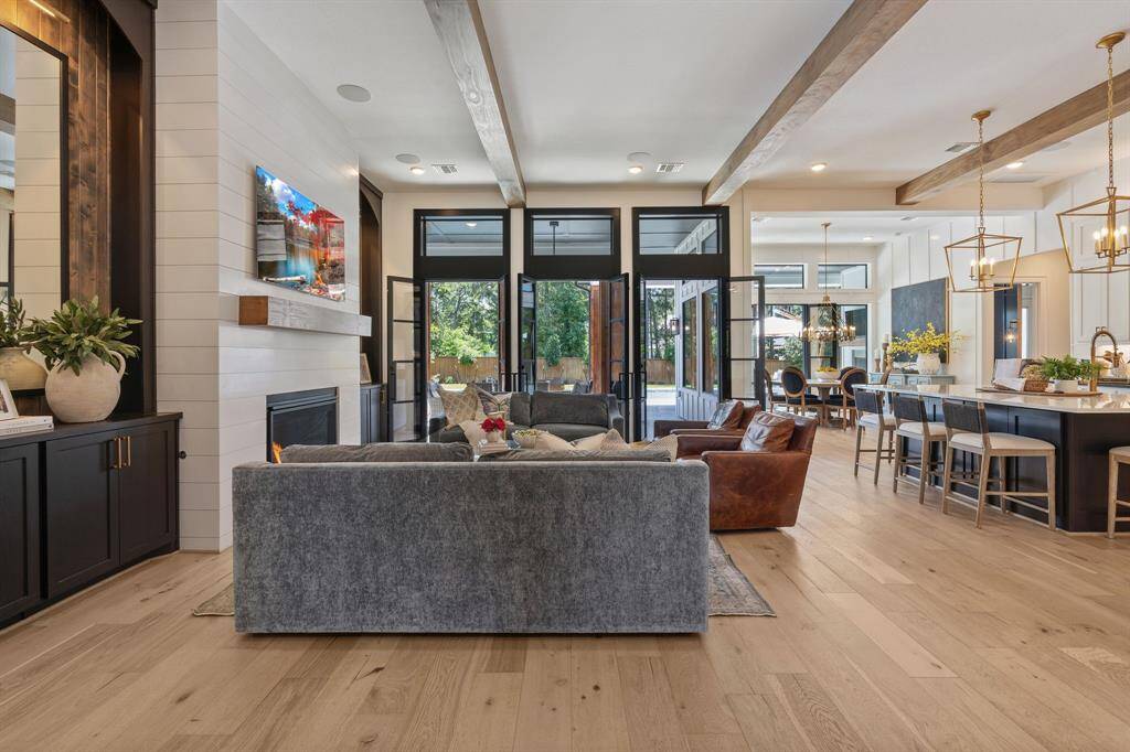 Light-filled and luxurious, this spacious living area features wide-plank hardwood floors, wood-beamed ceilings, and a stunning shiplap fireplace with custom built-ins. A full wall of glass doors swing open to the covered patio and pool, effortlessly blending indoor comfort with outdoor entertaining.