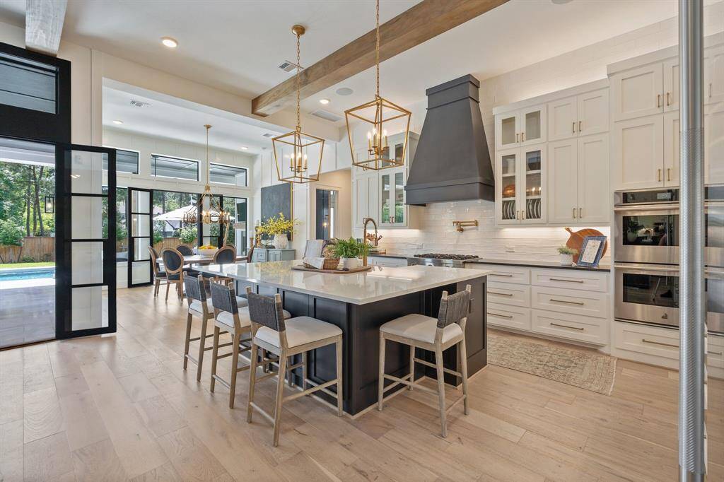 Gourmet kitchen seamlessly connects to the dining and living spaces, creating an open-concept flow ideal for entertaining. Statement pendant lighting, a bold vent hood, and an oversized island add visual impact, while walls of black-framed doors swing open to extend gatherings effortlessly to the outdoor oasis.