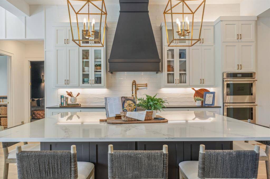 Sophisticated and functional, this chef’s kitchen boasts gleaming quartz countertops, a bold custom vent hood, soft-close cabinetry with glass inserts, and designer pendant lighting. The spacious island with seating anchors the room—perfect for gathering, prepping, or casual dining.