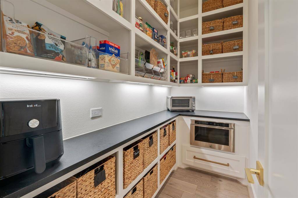 Walk-in pantry with custom built-in shelving, abundant storage, built in microwave and sleek black countertops will make it easy to organize and store all of your kitchen necessities.