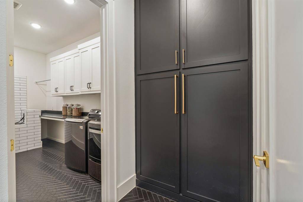 Coming in from the garage is the MUD room w/ great storage that has an entrance into the massive laundry room. Black herringbone tile flooring adds a sophisticated touch, while the laundry area includes overhead storage surrounded by white subway tile, and a spacious countertop for folding or organizing. There is also a dog wash perfect for your pets!