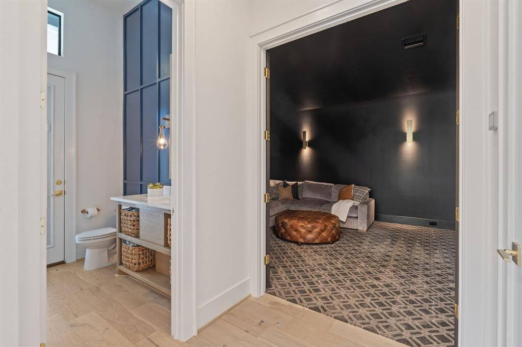 On the left is a stylish bathroom with modern gold accents, a minimalist vanity with open shelving with access to the outdoor living areas, and a bold navy-blue accent wall with trim detail. On the right is a cozy media room with deep charcoal walls, patterned carpet, subtle wall sconces.