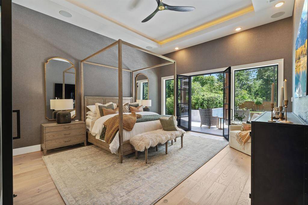 The serene primary suite features a tray ceiling, 12 ft ceilings with ambient lighting and direct access to the patio through beautiful French doors, creating a luxurious indoor-outdoor retreat.