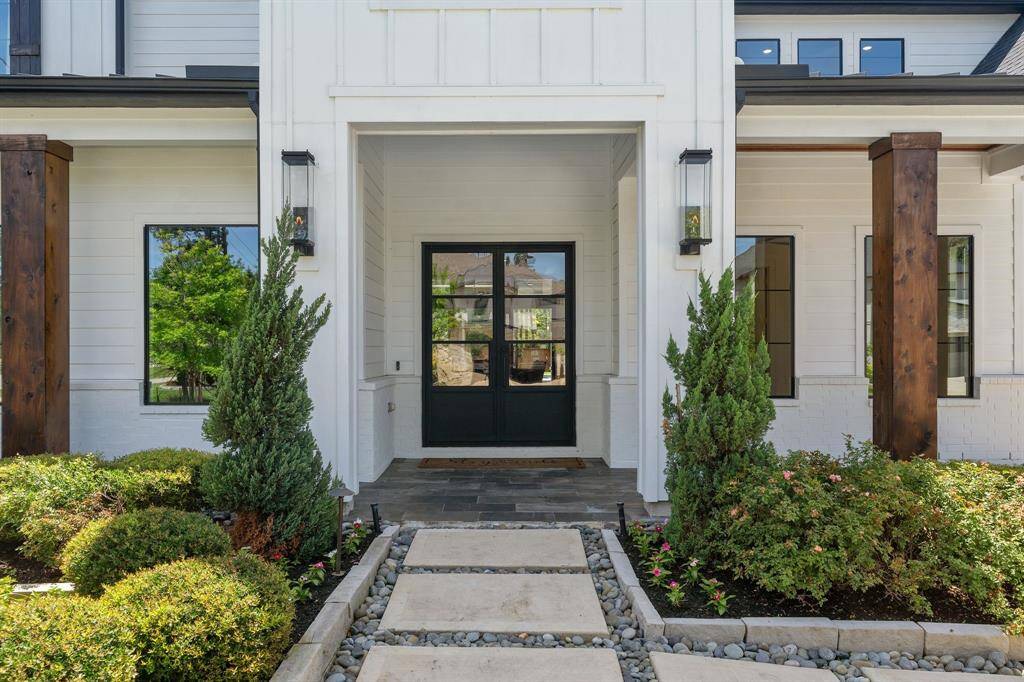 A grand first impression begins at the double glass front doors, framed by rich wood columns, modern gas lanterns, and lush landscaping. The stone pathway with river rock accents adds a custom touch, guiding guests into the heart of this exquisite home.
