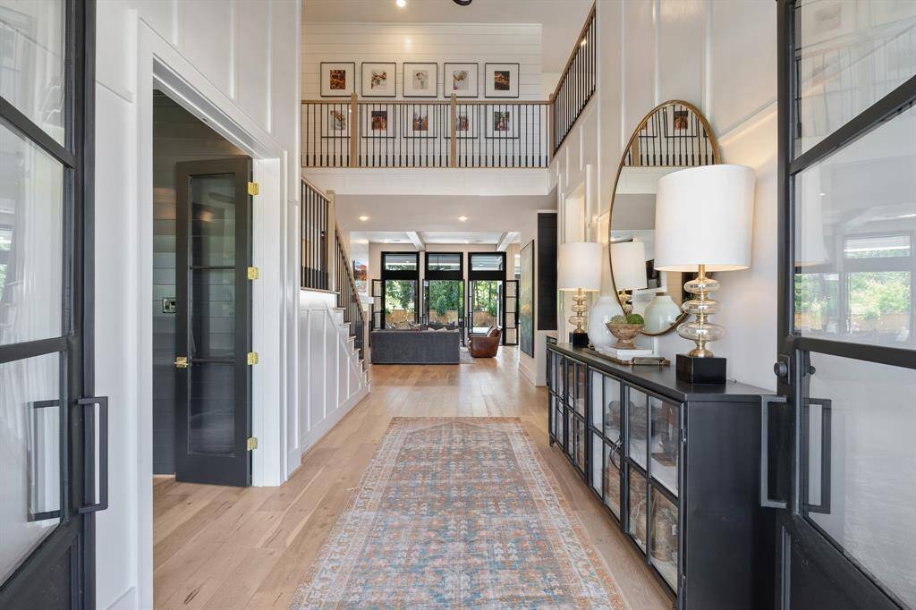 Step inside to a soaring two-story foyer with rich millwork, wide-plank hardwood floors, and abundant natural light. Framed by sleek black steel doors and flanked by designer lighting and decor, this striking entry sets the tone for the elegant style and flow of the home beyond.