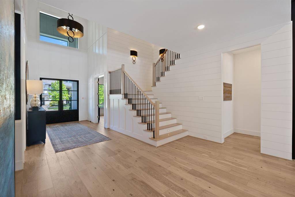 The front entry opens to a spacious two-story foyer with clean board and batten walls with shiplap walls leading up the stairs, modern light fixtures, and gorgeous wide-plank hardwood floors. The staircase features sleek iron balusters and natural wood rails, adding architectural interest and a graceful transition to the second level.