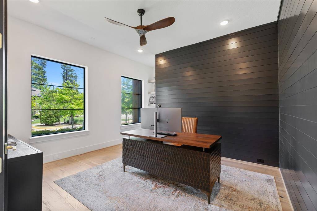 Tucked just off the entry, this stylish home office features dark shiplap accent walls, sleek modern windows with black trim, and plenty of natural light. To the left is a custom built in cabinet with an outlet and shelves. A perfect space for remote work, creativity, or quiet study—designed with both function and flair.