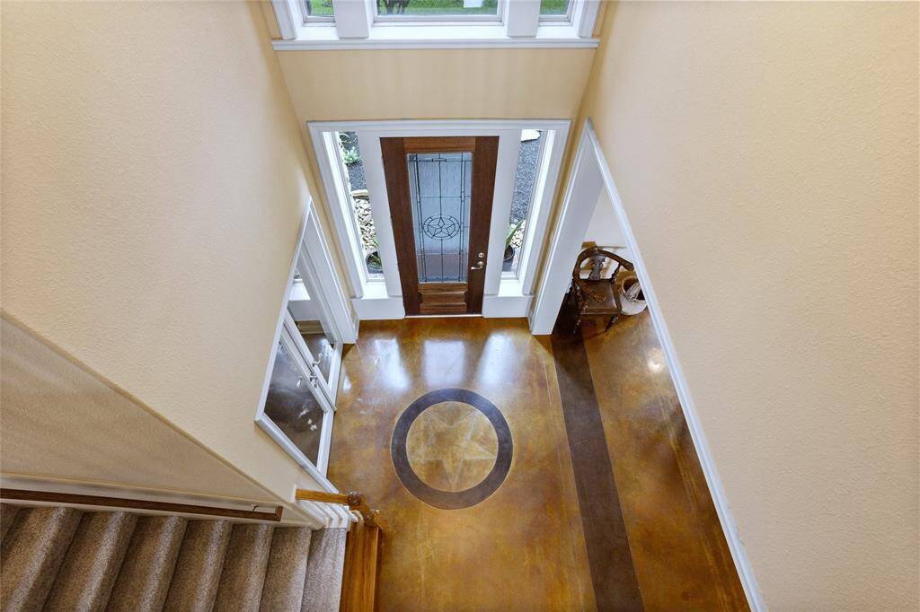 The stunning view from upstairs overlooks the grand entryway, where a bright and welcoming atmosphere greets you. The decorative wooden front door, with its elegant glass panels, makes a striking first impression. Large windows flood the space with natural light, highlighting the polished flooring and enhancing the overall sense of openness and warmth.