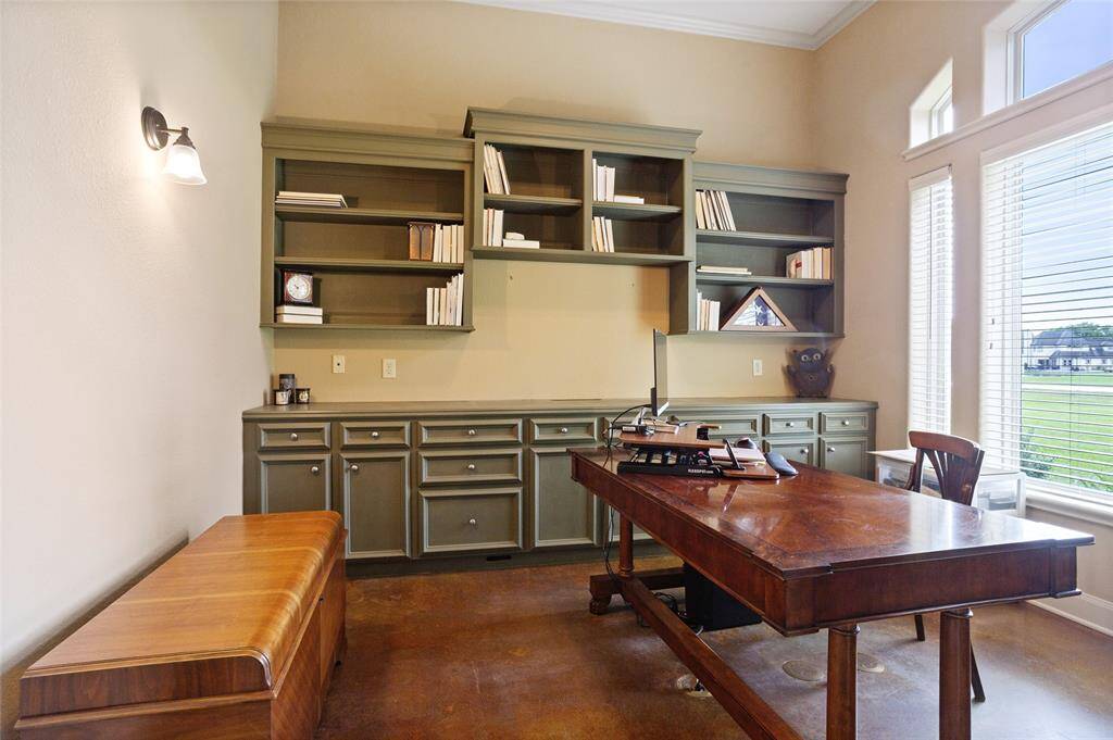 This home office offers a highly functional workspace, featuring large windows that fill the room with natural light. It also includes built-in shelving, ample cabinetry for efficient storage, and convenient floor plugs for easy desk setup.