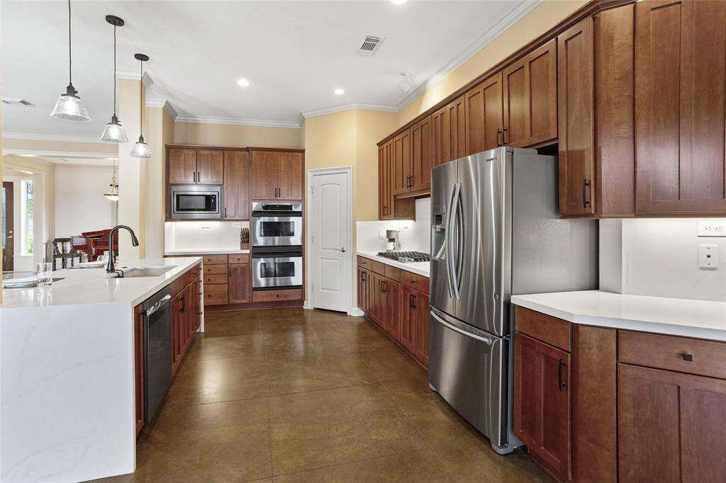 This modern kitchen features new quartz countertops, stainless steel appliances, and abundant wood cabinetry, accented by undermount lighting. It also includes a new 5-burner gas range stove and double ovens. The spacious layout showcases a striking waterfall island and stylish pendant lighting, creating a functional and inviting space ideal for both cooking and entertaining.