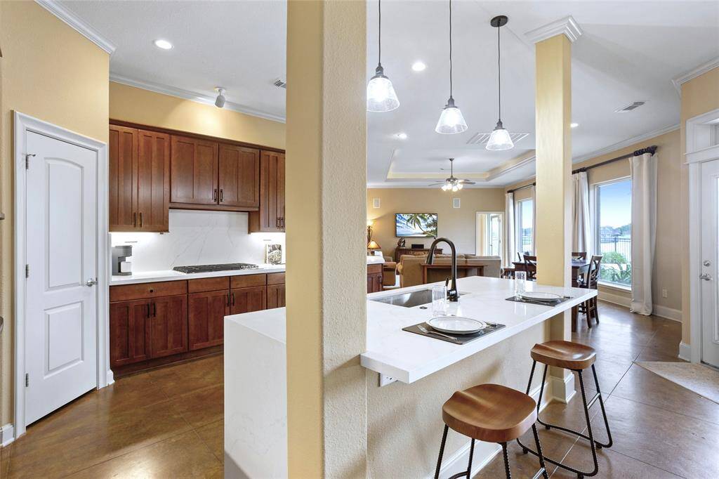 This open-concept kitchen boasts a modern design, featuring a sleek waterfall island with bar seating, stylish pendant lighting, and rich wood cabinetry. Large windows offer stunning views of the pool and lake, filling the space with an abundance of natural light.