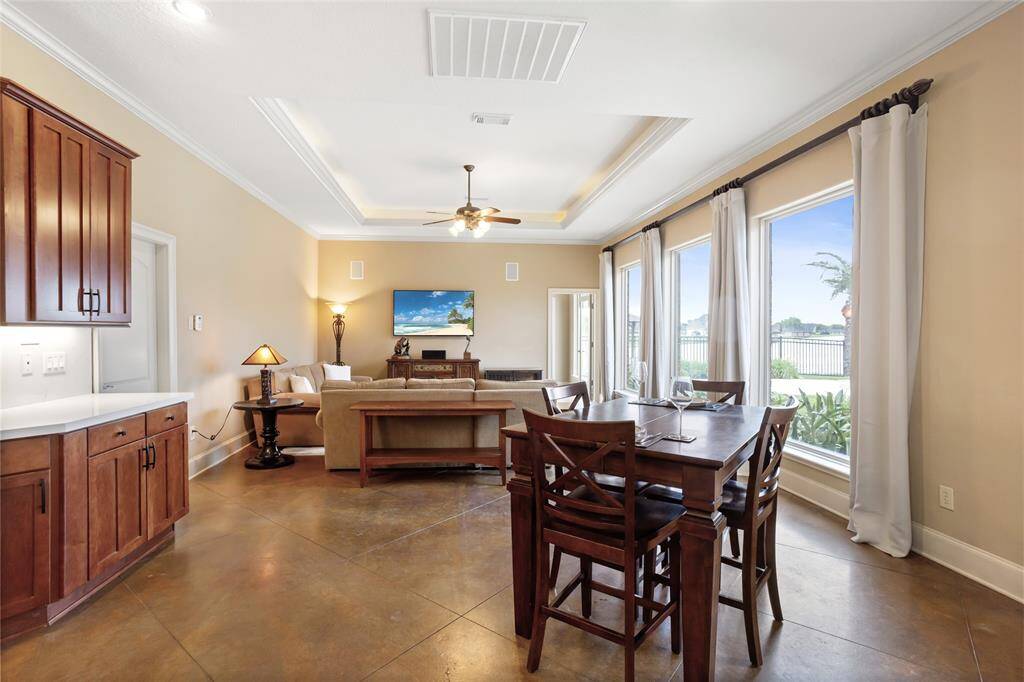 This open-concept family room is filled with abundant natural light from the floor-to-ceiling windows. Elegant tray ceilings add a touch of sophistication, while a cozy seating area creates the perfect space for relaxation and gathering.