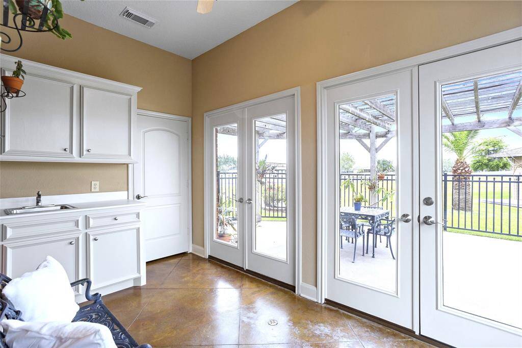The Sunroom, located off the Family Room, features white cabinetry with a sink, a storage closet, and a floor drain, offering both practicality and style. Glass doors lead to a second patio, where you’ll find seating under a pergola and a fenced yard surrounded by waterfront views.