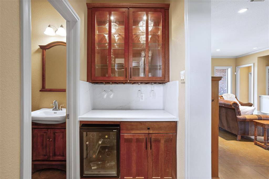 The Dry Bar features a built-in bar area with rich wooden cabinetry, glass front doors, a wine fridge, and sleek quartz countertops, offering a stylish and functional space for entertaining.