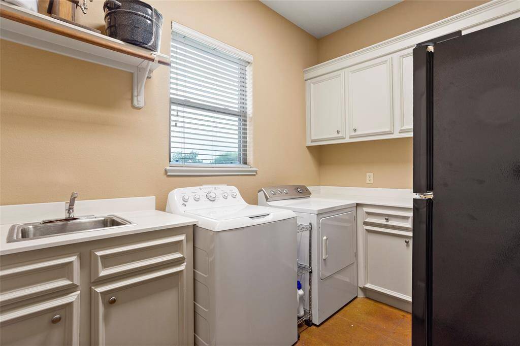 This oversized laundry room offers ample cabinetry for storage, a sink, generous counter space, and electrical and water hookups for an extra refrigerator. A window fills the room with natural light, making it both functional and bright.