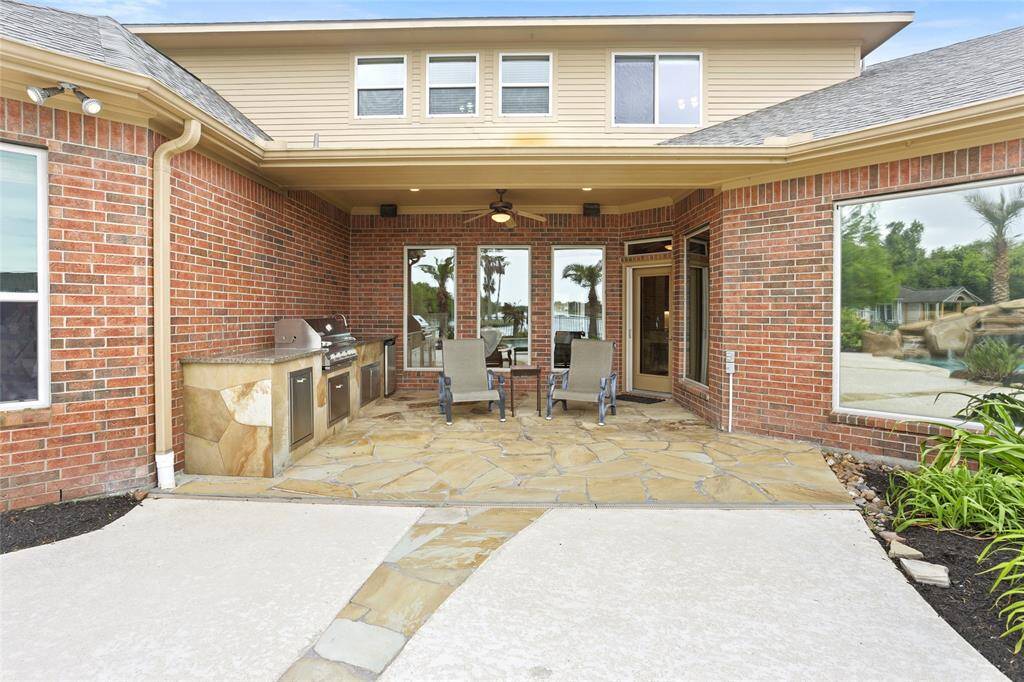 Charming backyard patio with a built-in outdoor kitchen that includes a grill, minifridge and convenient storage. The area is paved with flagstone and offers a seating area. Tinted, mirror-effect windows add privacy while reflecting the surrounding landscape for a polished, sophisticated look.