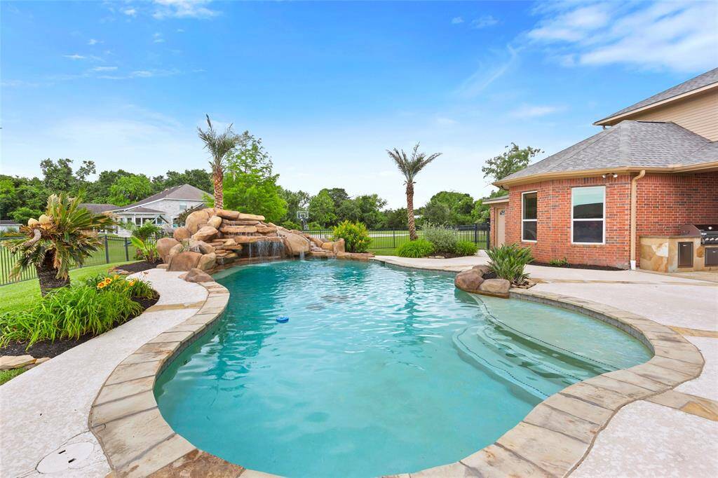 This stunning backyard oasis features mature landscaping and a resort-style pool complete with a rock waterfall, slide, grotto, sundeck, and built-in umbrella holders. The cool deck surrounds the pool area for added comfort, and an outdoor half bathroom provides added convenience for guests.