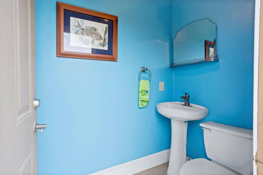 The outdoor pool bathroom features vibrant blue walls, a classic pedestal sink, and a wall-mounted mirror, offering a cheerful and convenient space for guests.