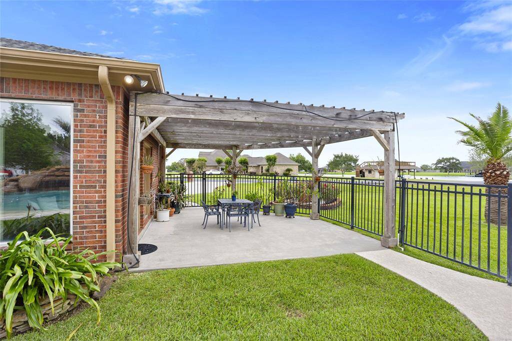 Enjoy outdoor dining on this charming backyard patio, shaded by a rustic wooden pergola. The space is enclosed by a wrought iron fence and offers picturesque lakeside views, creating a peaceful and inviting setting for alfresco gatherings.