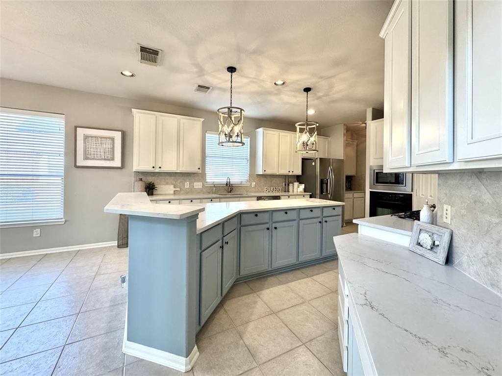 This recently updated island kitchen features a spacious layout with quartz counters, painted cabinets, a large island w/breakfast counter, and stylish pendant lighting, creating a bright and inviting atmosphere.