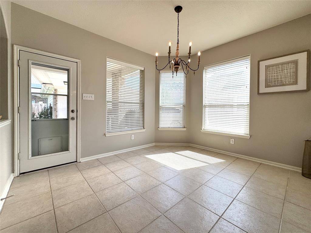 Bright dining area with large windows, neutral tile flooring, and a stylish chandelier. There's a door leading to an outdoor space and easy access to the covered patio and detached garage.