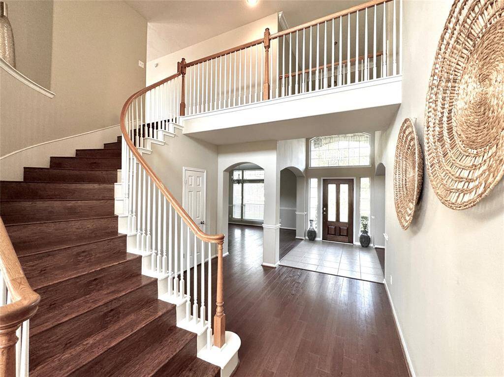 Spacious and inviting entry with a beautiful curved staircase and rich wood flooring. The high ceilings and large windows offer plenty of natural light, and the open layout provides a welcoming entrance to the home.