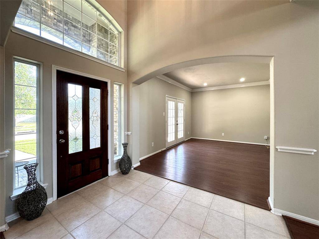 This inviting entryway features a wood and glass door with window surrounds. The arched doorway opens into a spacious home office.
