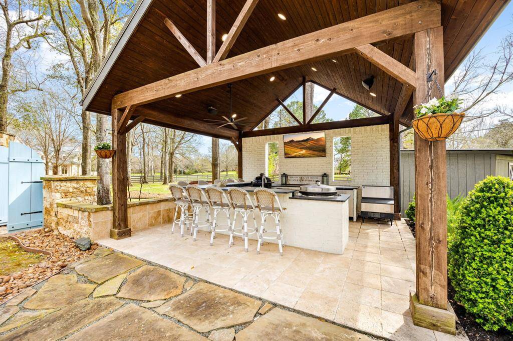 This beautiful outdoor kitchen is showcased by wooden beams and has ample bar seating. Built-in grills of all varieties will certainly please all your outdoor chefs. Featuring tiled flooring, wood ceiling, ceiling fan, speakers, and a mounted tv to create an inviting space for outdoor entertaining.