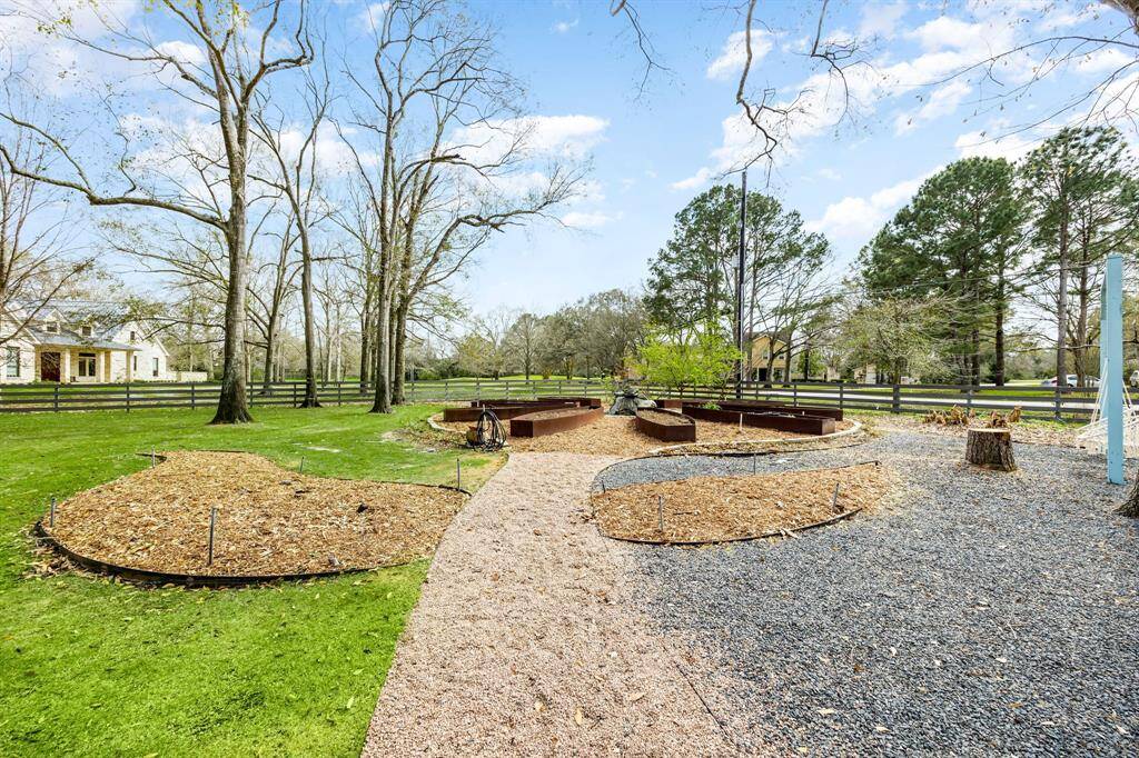 The spacious backyard features a custom-designed and landscaped garden with multiple raised beds in the shape of a flower petal lead by gravel paths. The area is surrounded by mature trees and a wooden fence, offering a serene and private outdoor space.