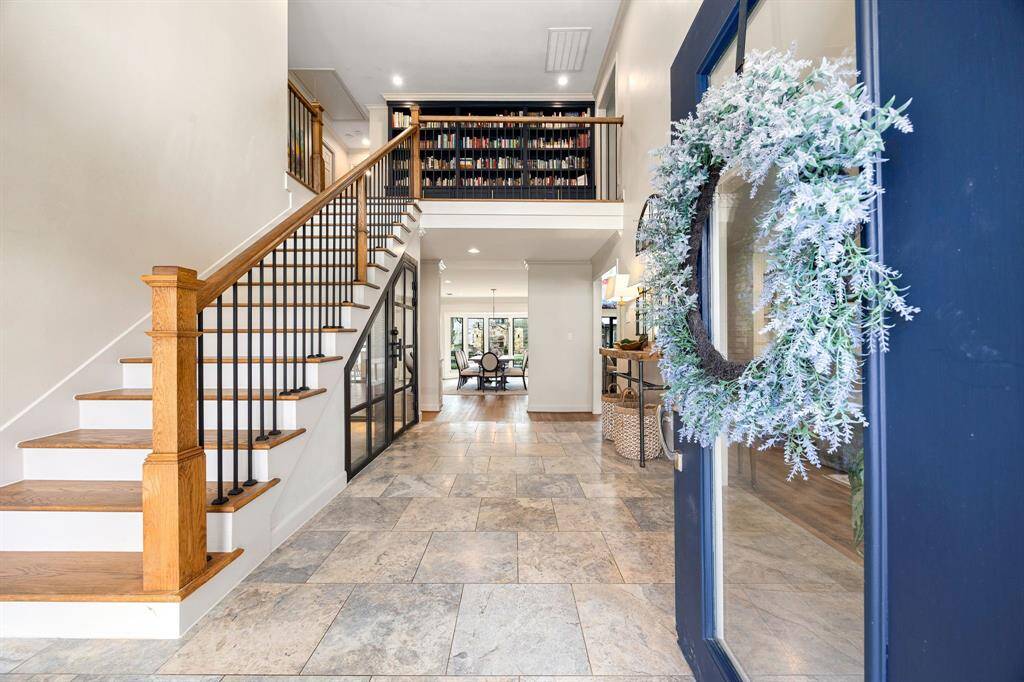 A grand double-door entry welcomes you with elegant travertine flooring and a wine closet tucked beneath the stairs. To the right, the formal dining room features a cozy fireplace and seamless flow into the living area, creating the perfect setting for entertaining and holiday gatherings.